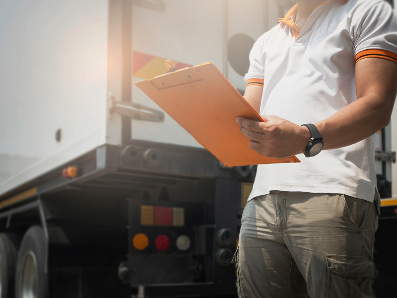motorista-de-caminhao-escrevendo-papel-na-prancheta-em-pe-com-o-caminhao-de-reboque-manutencao-e-inspecao-de-seguranca-veicular
